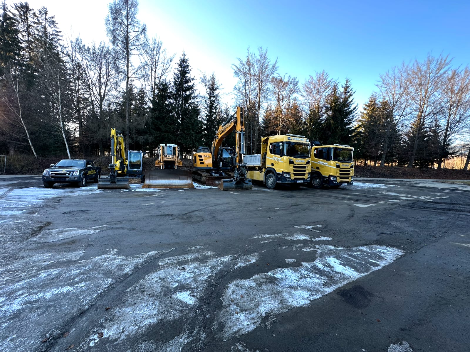 Eine Gruppe von Baumaschinen, darunter Bagger und Lkw, steht auf einem Parkplatz.